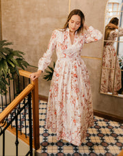 Woman in a floral dress standing in a room with a mirror and plant.