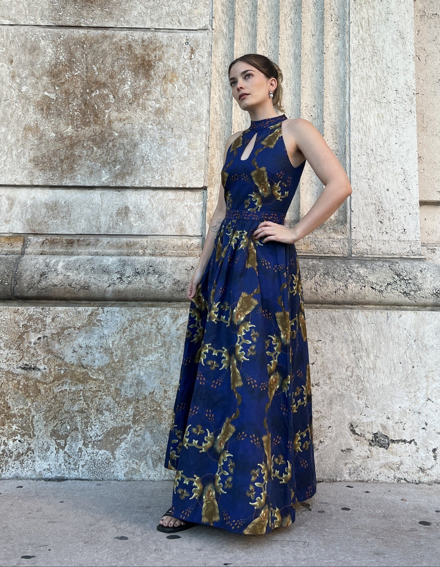 Woman in a blue and gold dress standing against a stone building.
