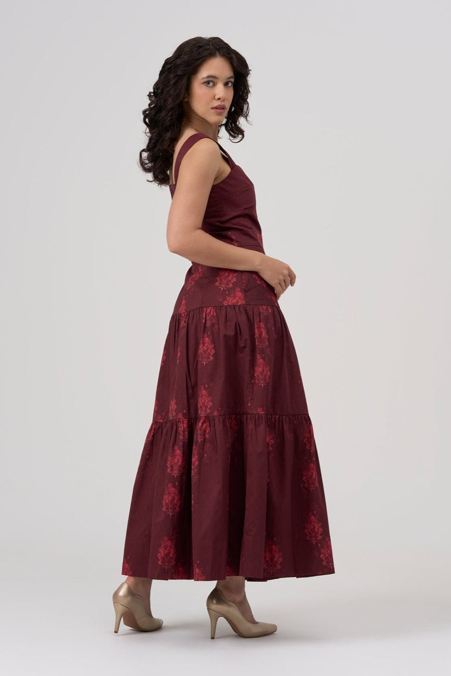 Woman wearing a bordeaux maxi dress with floral patterns on a white background