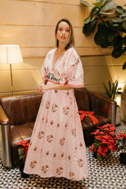 Woman in a floral dress standing in a room with a brown couch and decorative plants.