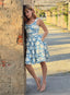 Diva Thea model wearing a blue and white Athena hemp and cotton print sleeveless dress leans against a rustic concrete pillar in an outdoor covered walkway in Miami.