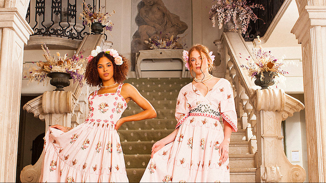 Two women in floral dresses standing on a staircase with decorative elements.