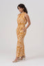 Women’s wide-leg halter jumpsuit in natural linen, featuring Diva Thea’s Amber Radiance print in gold, amber, and deep ochre. Adjustable halter neckline, fitted natural waist without elastic, tiered wide-leg silhouette, and side pockets. Suitable for weddings, cultural events, warm-weather dinners, and other occasion dressing.